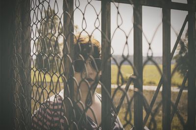 Portrait of woman looking through chainlink fence