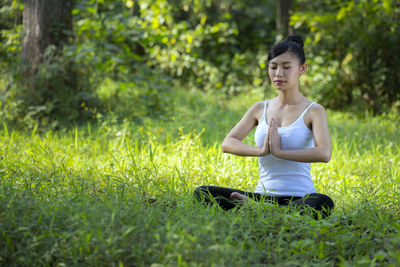 Full length of woman meditating while sitting on grassy field