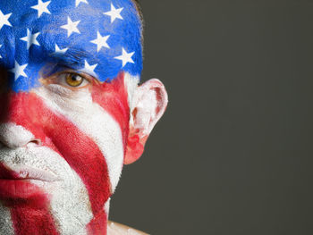 Close-up portrait of sad man with american flag body paint against gray background