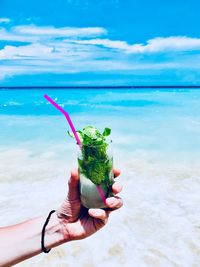 Person holding ice cream at beach against sky