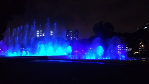 Illuminated city by sea against blue sky at night