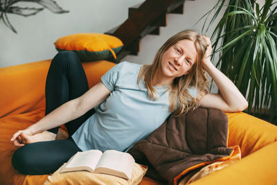 A young woman is sitting on a comfortable sofa in the room and smiling, 