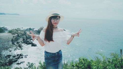 Portrait of woman gesturing peace sign while standing against sea
