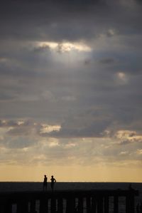 Silhouette of people on beach against cloudy sky