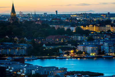 Illuminated cityscape by sea against sky at sunset