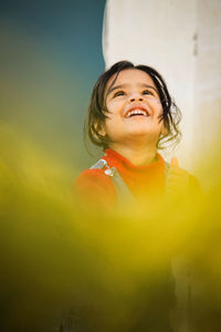 Thoughtful girl smiling while standing against wall