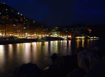 Illuminated buildings by sea against sky at night