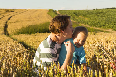 A happy little boy and his teenage brother are walking in a wheat field on a bright, sunny day.
