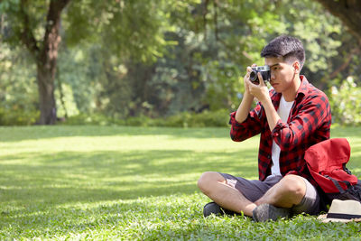 Man photographing with camera sitting on grass