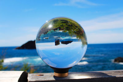 Close-up of crystal ball on sea against blue sky