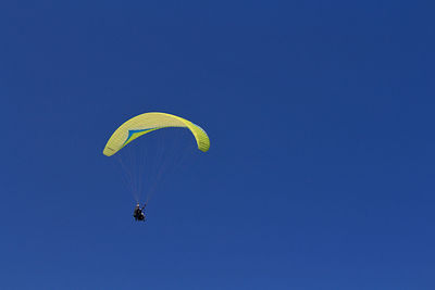 Low angle view of person paragliding against clear blue sky