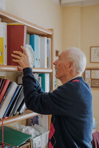 Senior man keeping book on shelf at home