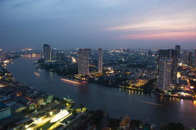 High angle view of illuminated buildings by river against sky
