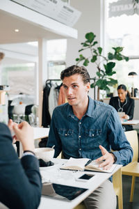 Businessman discussing with colleague while sitting at desk in office cafeteria