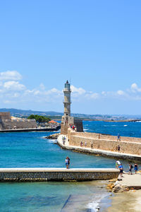 Lighthouse by sea against blue sky