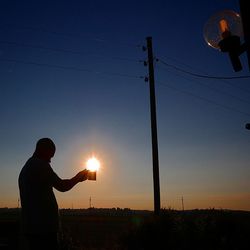 Silhouette man standing by electricity pylon against sky during sunset