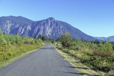 Road leading towards mountains against clear blue sky