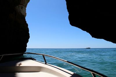 Boat sailing in sea against clear blue sky from a cave