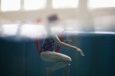 Side view of woman exercising with noodle float in swimming pool