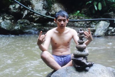 Full length of shirtless man sitting in river