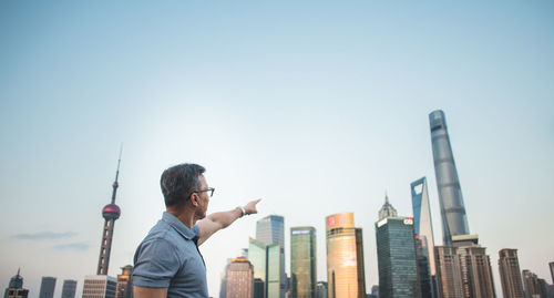 Full length of man holding modern buildings against clear sky