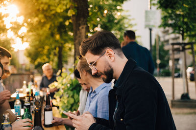 Young man using phone while sitting female friend at social gathering