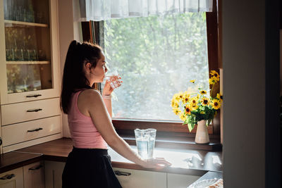 Young woman drinking water from glass in the kitchen. caucasian female model holding transparent