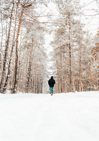 Rear view of man walking on snow covered land during winter