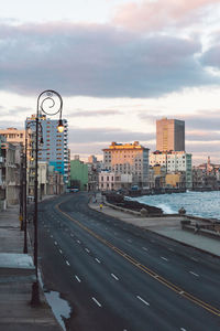 Road by buildings against sky during sunset