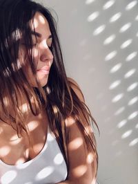 Sunlight falling on beautiful young woman with eyes closed against wall