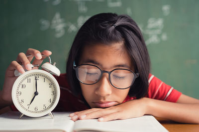 Girl with eyeglasses sleeping on book with alarm clock on table