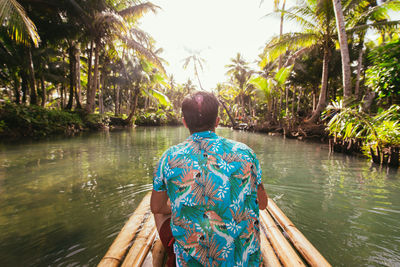 Rear view of man sitting on wooden raft in river