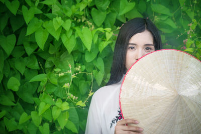 Portrait of smiling young woman with hat standing plants