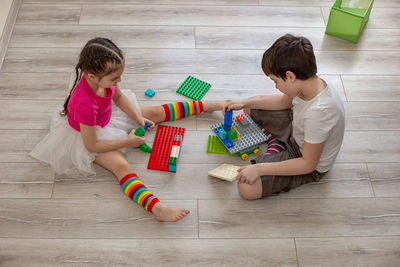 Two children, a boy and a girl, sit on the floor in room and play in plastic constructions