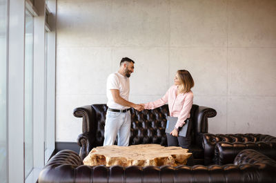 Business people shaking hand while standing by sofa