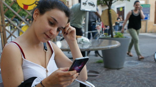 Close-up of thoughtful woman using mobile phone at sidewalk cafe 