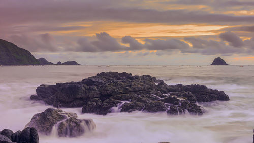 Rocks on sea shore against sky during sunset