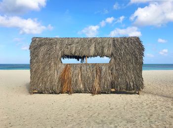 Thatched roof shade at sandy beach against sky