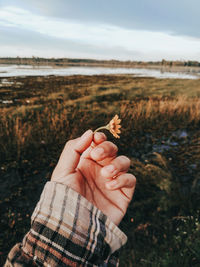 Midsection of person holding plant on land against sky