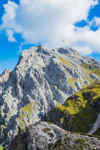 People on rocks by mountain against sky