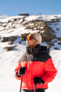 Una mujer afroamericana con bastones de esquí de pie en una montaña nevada durante el invierno