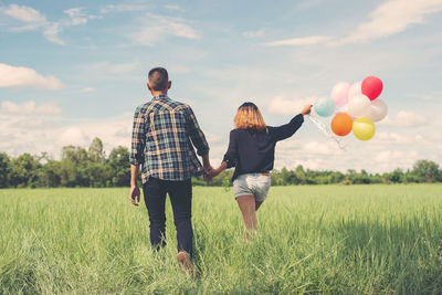 Rear view of people with balloons walking on field against sky