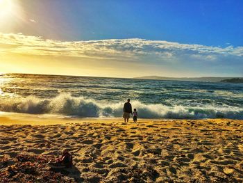 Rear view of silhouette father with son standing at beach against sky during sunset