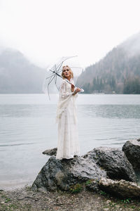 A beautiful young woman bride in a wedding lace dress stands in the middle of a lake and mountains