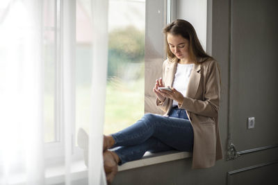 Work-life-balance, caucasian female manager on the windowsill in the hall with smartphone