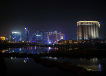 Illuminated buildings by river against sky at night