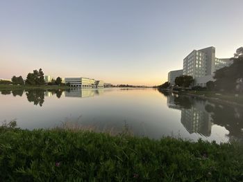 Scenic view of lake by buildings against sky during sunset