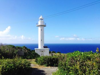 Lighthouse by sea against blue sky