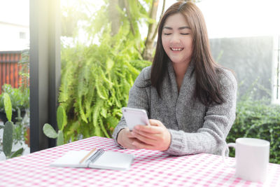 Young woman using phone while sitting on table