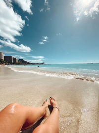 Low section of woman relaxing at beach against sky